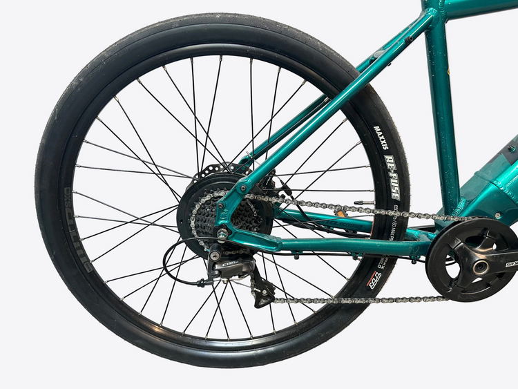 Close-up of a teal bicycle with chain and gear system on a light gray background