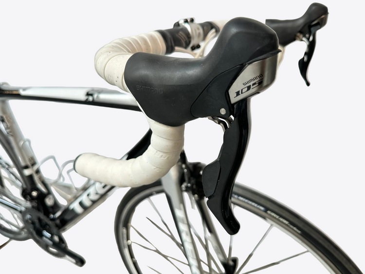 Close-up of bicycle handlebars with white grips and black levers against a light background