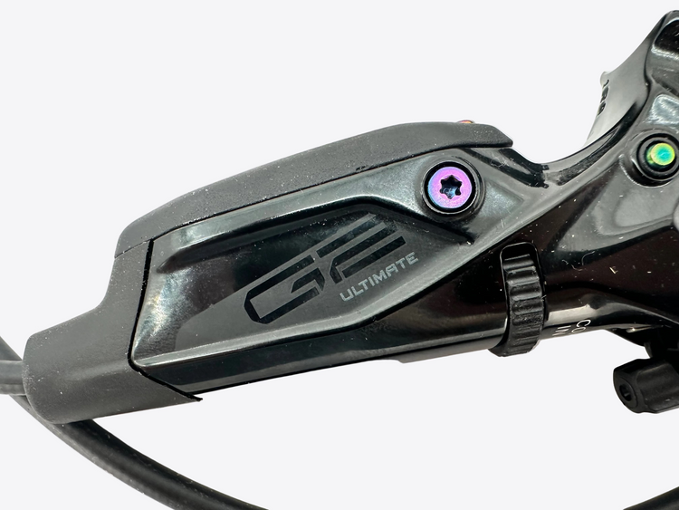 Close-up of a black hydraulic brake lever with 'G2 ULTIMATE' branding, featuring a purple accent screw and a green button on a white background.