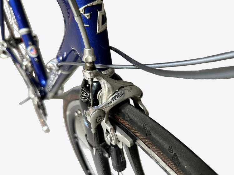 Close-up of a bicycle's front derailleur against a tiled wall.