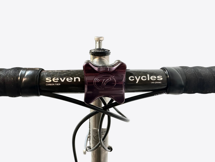 Close-up of bicycle handlebar with 'seven cycles' branding on a blurred indoor background
