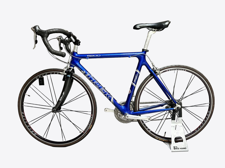 Blue bicycle with black components against a gray brick wall.