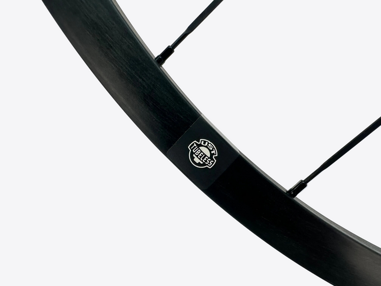 Close-up of a black bicycle rim with a brand logo on a light gray background