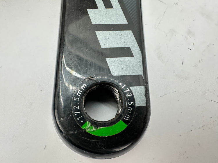 Close-up of a bicycle crank arm with brand logo on a light gray background