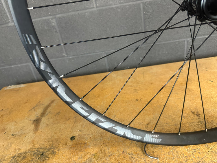 Bicycle wheel with carbon fiber rim on a wooden surface and gray tiled wall background
