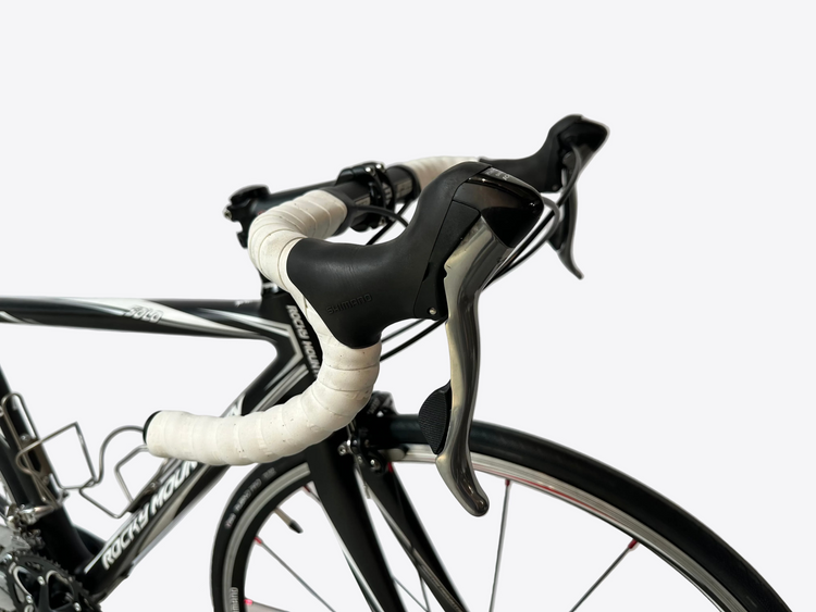 Close-up of a bicycle handlebar with white grips and black brake levers against a light background