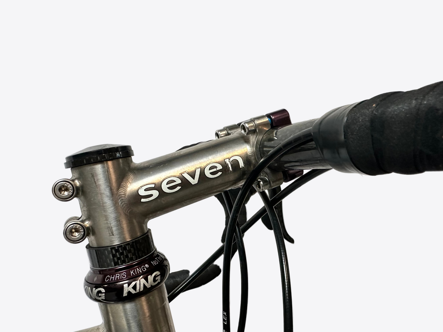 Close-up of a bicycle handlebar with 'seven' branding on a light gray background