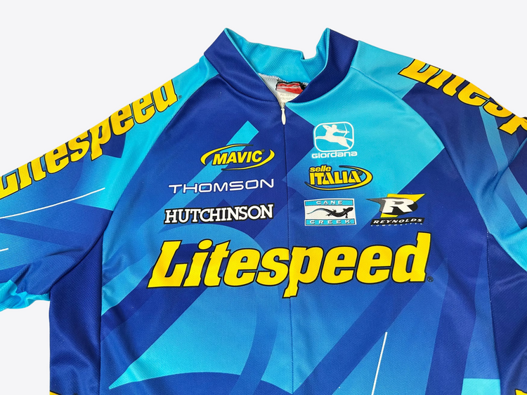 Blue cycling jacket with various brand logos on a beige background