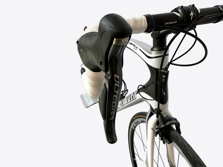 Close-up of a bicycle with a white frame and black components, leaning against a wall.