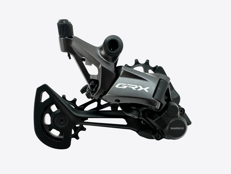 A Shimano GRX rear derailleur in matte black and dark gray, photographed on a light gray background.