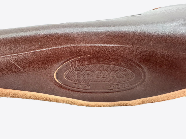 Close-up of a brown leather saddle with 'Brooks' branding on a white background