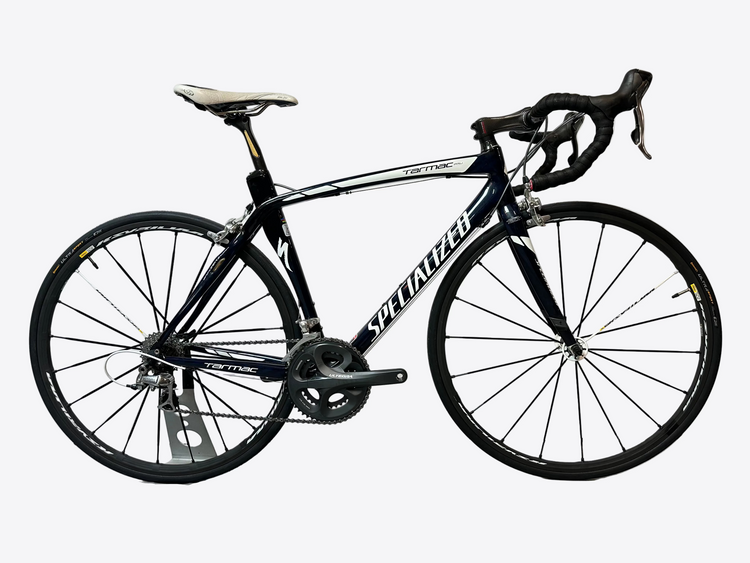 A black Specialized road bicycle with drop handlebars, a white saddle, and black wheels, displayed on a stand against a white backdrop.