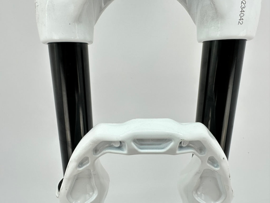Close-up of bicycle forks with white plastic housing and black metal components on a light gray background.