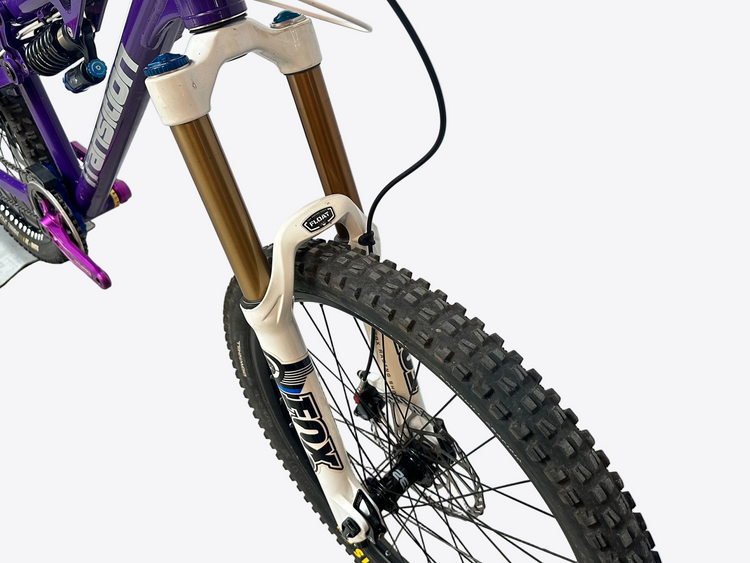 Close-up of a bicycle with a purple frame and Fox suspension fork on a light gray background