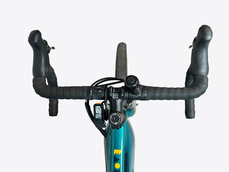 Bicycle handlebars with a digital display against a light gray wall.
