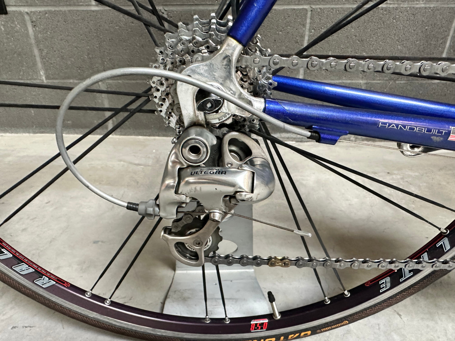 Close-up of a bicycle's gear system with a blue derailleur on a gray floor.