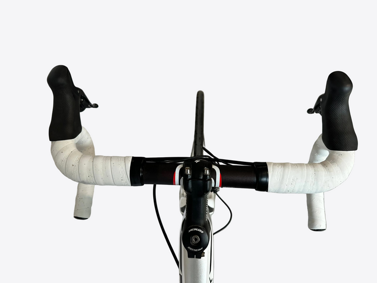 Close-up of a bicycle handlebar with white grips and black ends on a concrete floor.
