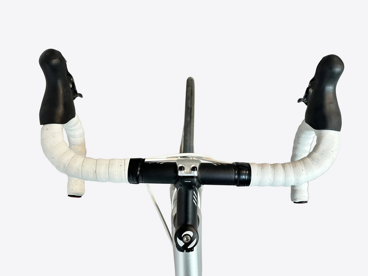 Close-up of a bicycle handlebar with white grips and black ends on a concrete floor.