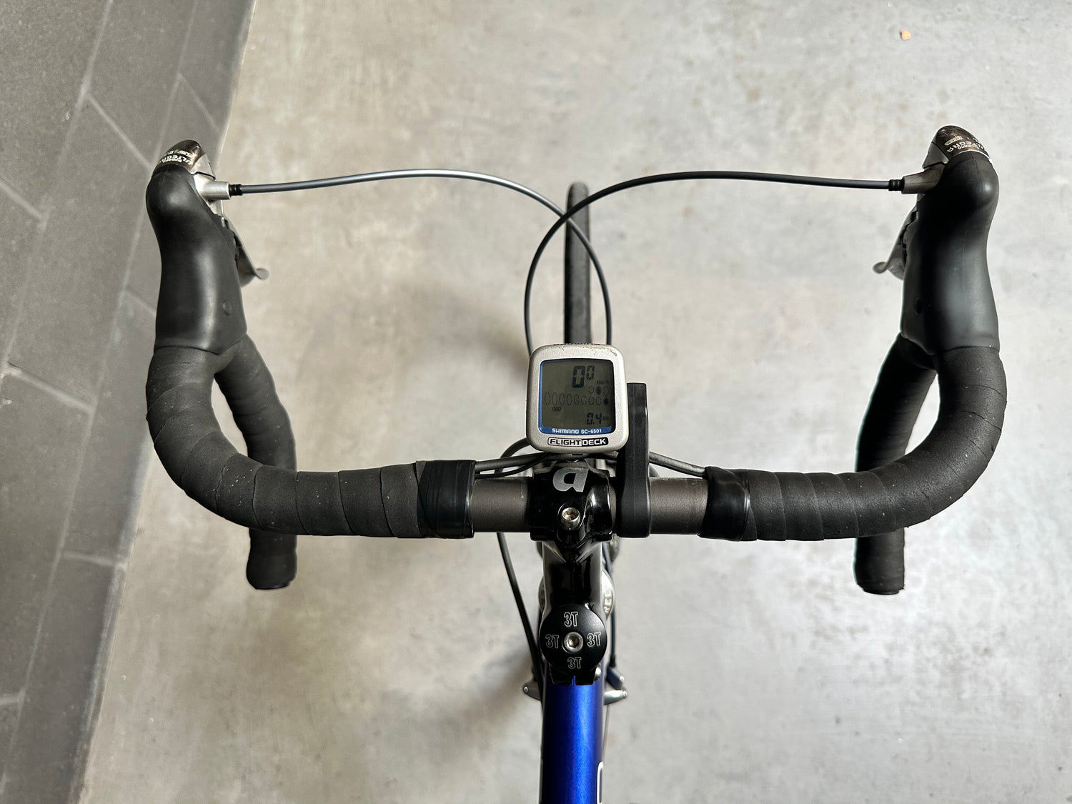 Bicycle handlebars with a digital display against a gray wall.