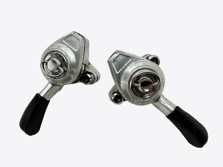 Two metal bike shifters with black handles on a white surface