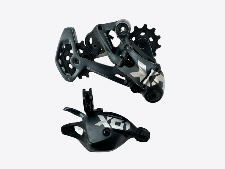 A black and silver X01 bicycle rear derailleur and matching cable guide shown on a light gray background.
