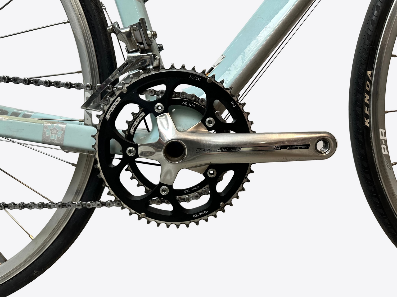 Close-up of a bicycle chainring and chain on a light blue bike with a white wall background.