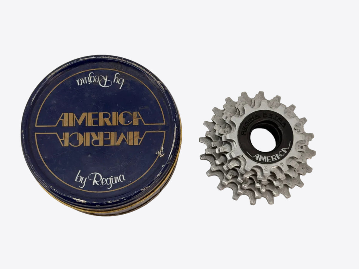 A vintage bicycle freewheel and its original blue and gold metal tin packaging, shown on a plain off-white background.
