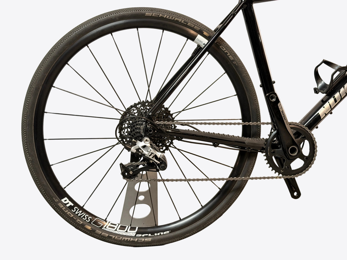 Close-up of a black bicycle wheel, rear cassette, chainring, and part of the black frame on a white studio background.
