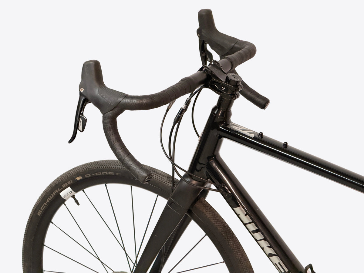 Close-up of a nukeproof gravel bike frame, handlebars, brake levers, and front wheel against a plain light background.
